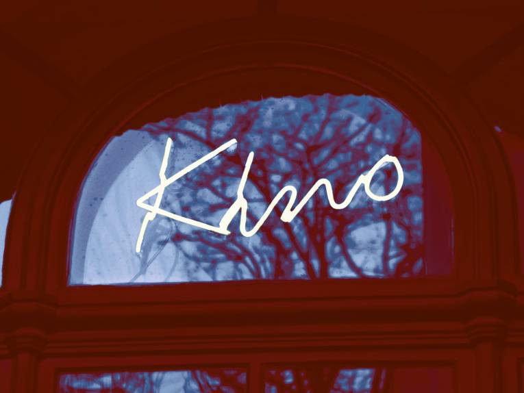 Die Leuchtschrift Kino im Fenster des Künstlerhauses in weiß. Der Hintergrund in Rottönen